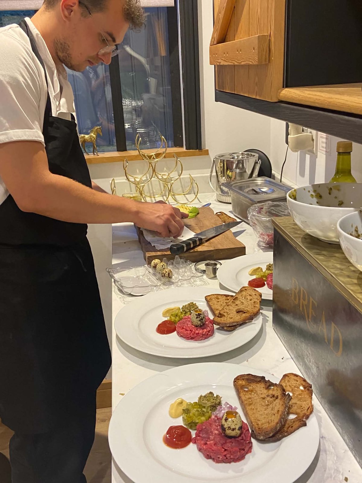 Chef Gergo Barna plating a row of beef tartare starters on a home kitchen worktop, knife in hand.