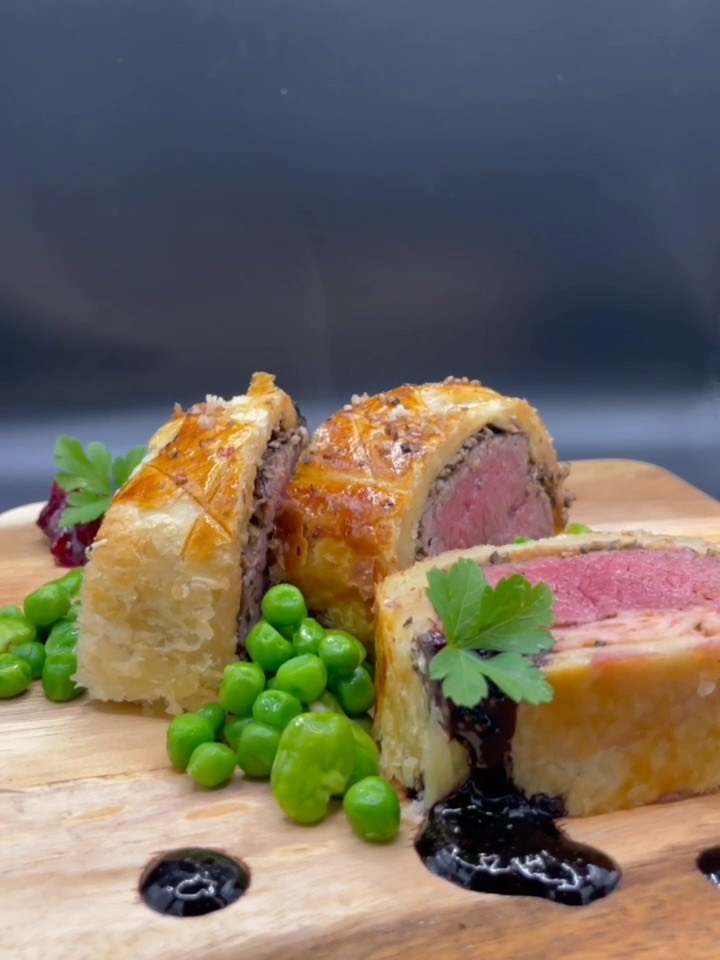 Slices of beef Wellington with a pink centre, plated with garden peas and a dark jus.